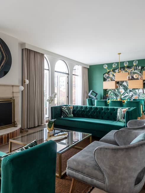 A sitting area with several emerald green couches, small grey chairs and plants.