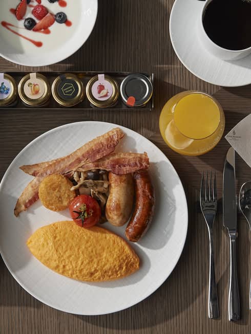 A variety of food on plates including sausage, eggs, fruit, croissant, pastries, jams, and coffee.