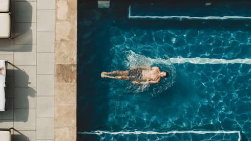 Woman laying in pool chair while man swims in pool.