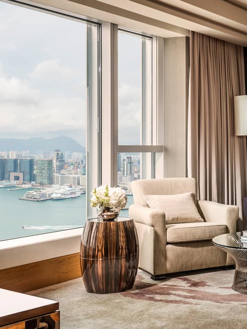 Plush armchair, shiny wood side table beside sunny picture window overlooking harbour, city