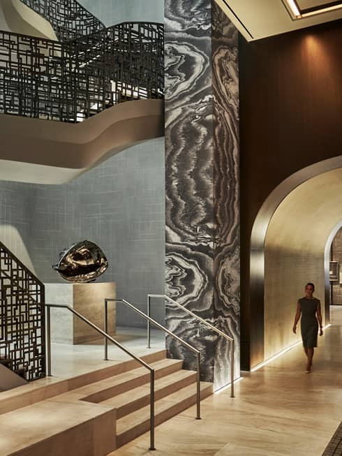 Woman walks down hall past tall black-and-white pillar, modern silver sculpture, black railings