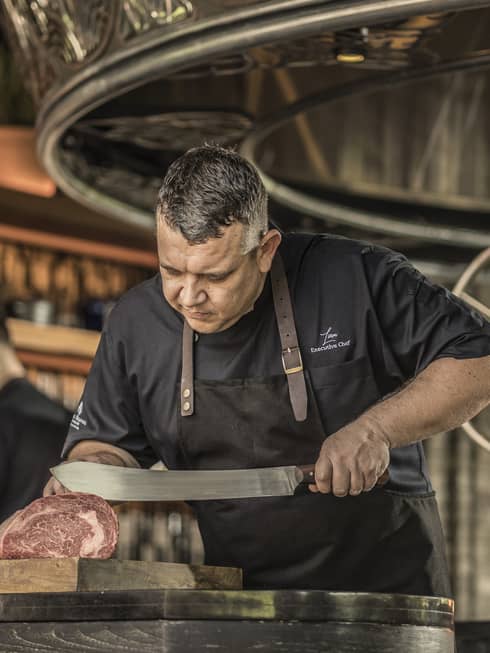 A chef slicing cured meat in an ornately decorated restaurant and bar