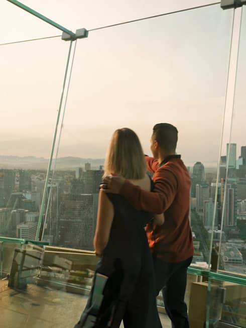 A man and woman walking in a tall building with glass walls looking out at a city.