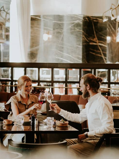 Smiling couple at table toasts with wine glasses in restaurant lounge
