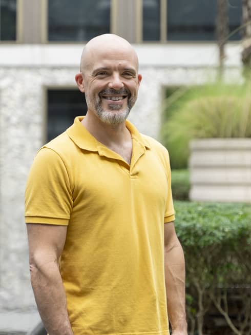 Smiling bald man with mustache and beard in yellow polo shirt poses outdoors