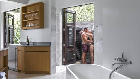 Interior view of small apartment with man and woman in swimsuits embracing in outdoor shower beyond