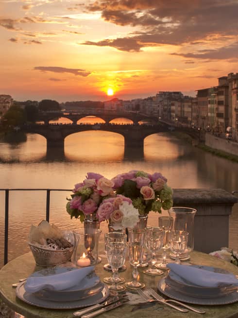 Pink roses in vases on formal dining table on bridge overlooking canal, sunset