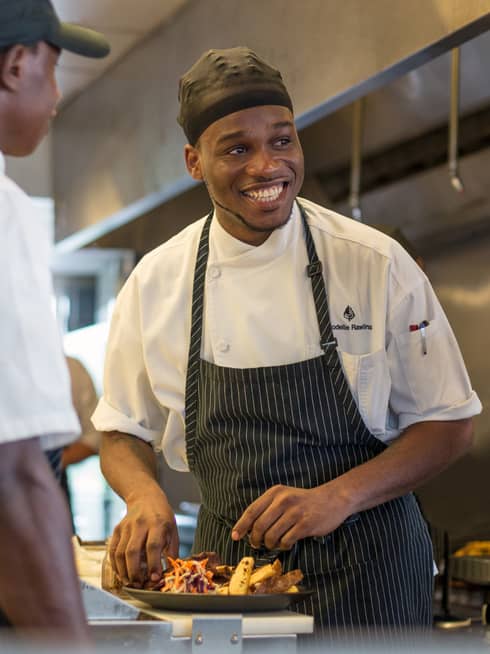 Portrait photo of smiling Sous Chef Rodelle Rawlins assembling food on plate