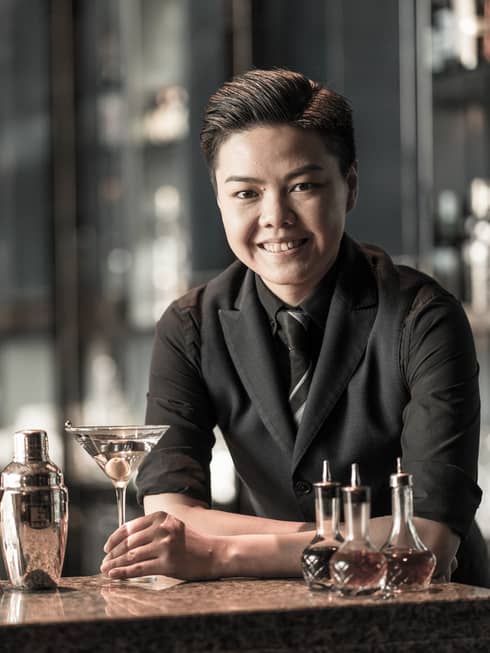 Photo of a female bartender, posing behind the bar with a martini
