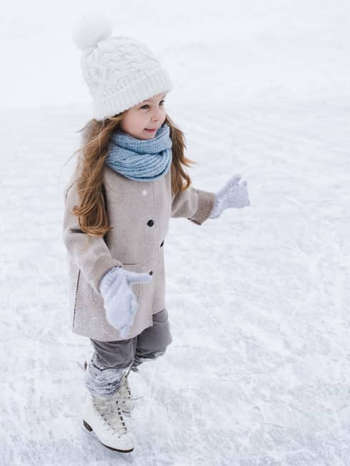 A small girl in winter clothes ice skating.