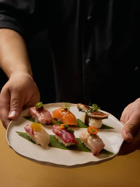 A person in a black shirt holds a plate with six different pieces of sushi.