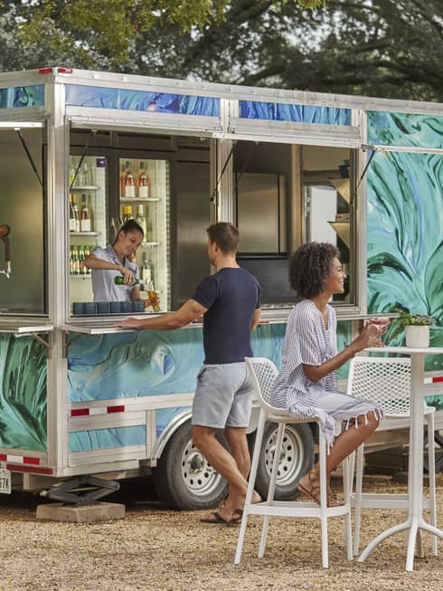 A food truck with people sitting by it outside.