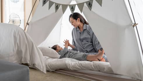 Parent and child in pyjamas playing together inside a cozy tent with bunting decorations