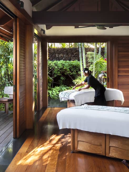 Spa staff spreads sheet on couples massage beds on open-air pavilion 