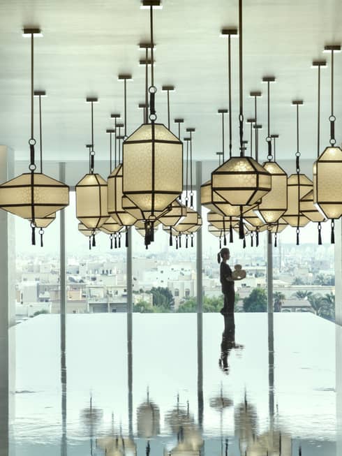 Hotel staff holds rolled white towels beyond large indoor swimming pool under dramatic lanterns