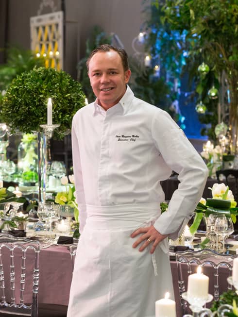 Executive Chef Omar Mallen in white uniform stands by banquet dining table
