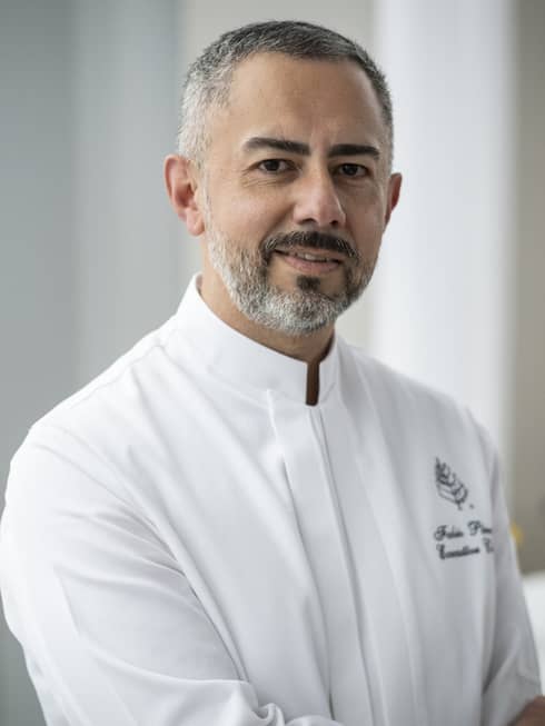 A chef with grey hair and short beard in a clean white chefs coat.