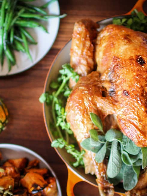 Roast turkey with fresh herbs on platter, presented on wood tabletop with gourds and green beans on white plate
