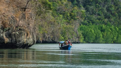Small blue boat on river under large cliffs, trees