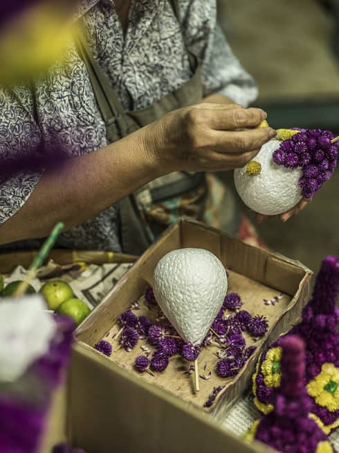 A florist places dried purple and yellow flowers in a pear-shaped floral foam to create traditional decorative pieces.