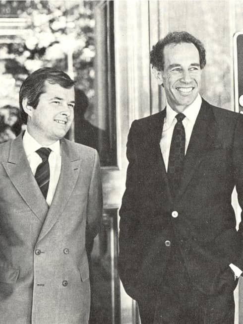 Black-and-white historic 1970s photo of two smiling men in suits by Four Seasons Hotel sign 