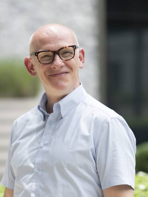 Smiling bald man in glasses and light blue button-up shirt poses outdoors