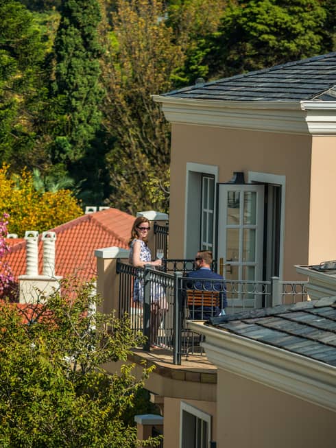 Looking down over corner of hotel roof at man and woman sipping cocktails on sunny balcony