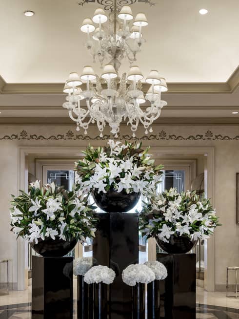Large white floral displays on black tables under crystal chandelier in hotel lobby