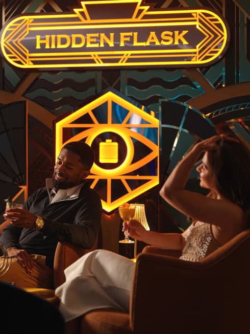 Two guests sitting in chairs beside a window and holding drinks