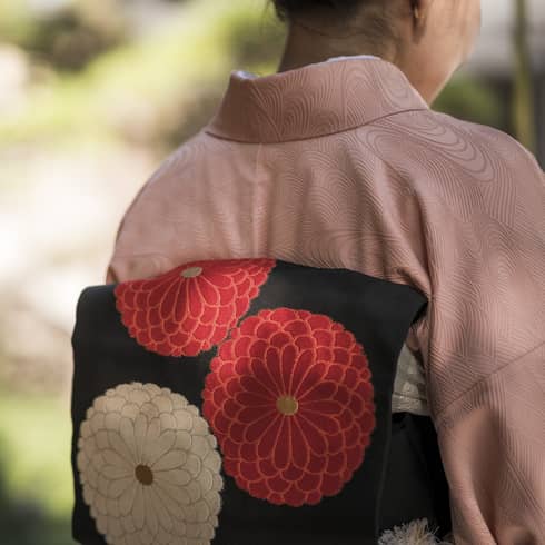 Back view of a person wearing a pink kimono with a black obi featuring red and white floral designs