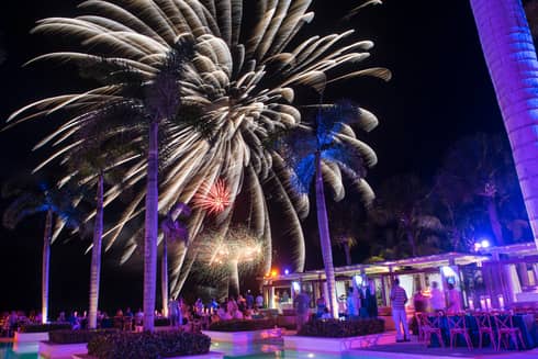 People around resort outdoor pool/bar watching fireworks in the night sky