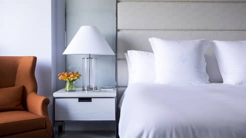 Midtown Deluxe Room close-up of crisp, white bed and linens, lamp next to orange accent chair 