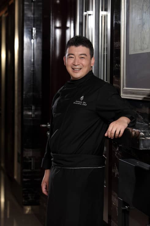 Portrait photo of Executive Chef Jackson Wu standing, smiling in black uniform