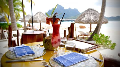 Fruity cocktail with tropical flower garnish on patio dining table by Bora Bora lagoon