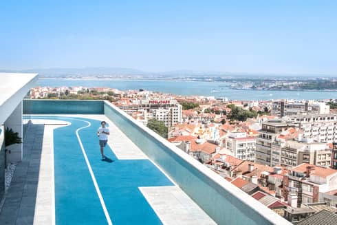 Man running on rooftop track, Lisbon city rooftops below