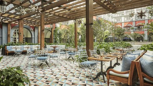Colourful tiles,  iron patio chairs with blue cushions, tables under awning on Zanaya terrace
