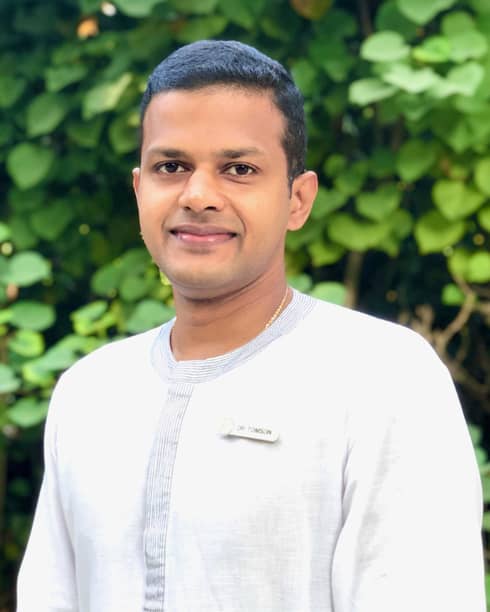 A smiling Dr. Arun K. Thompson in front of some greenery