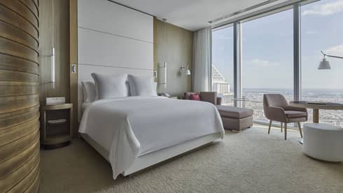 Bedroom with king bed, floor-to-ceiling headboard, arm chair and wall of windows