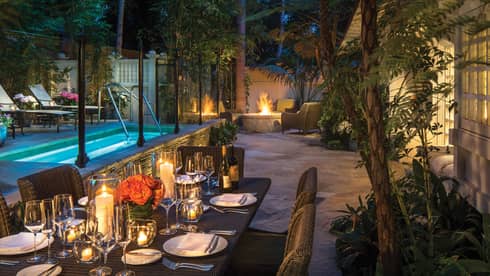 Ty Warner bungalow backyard candle-lit patio dining table by plunge pool, fire pit at night