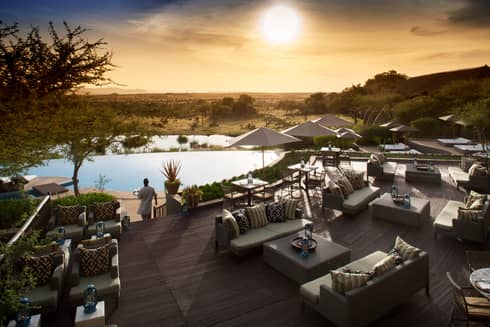 Server carries tray through Terrace Bar outdoor patio by lounge chairs, swimming pool at sunset