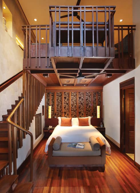 Resort room bed and bench beside winding wood staircase leading to second-level loft