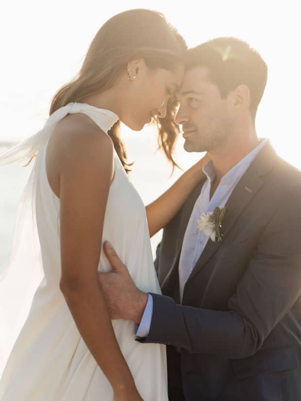 A bride and groom are touching foreheads as they hug in the sunlight.