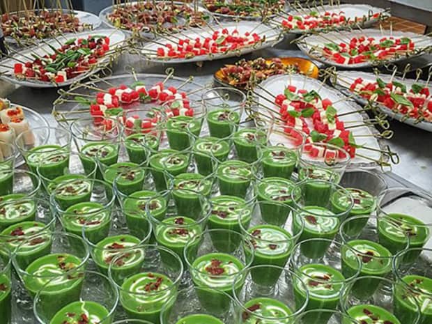 Buffet table with green smoothies in glasses, fruit skewers on platters