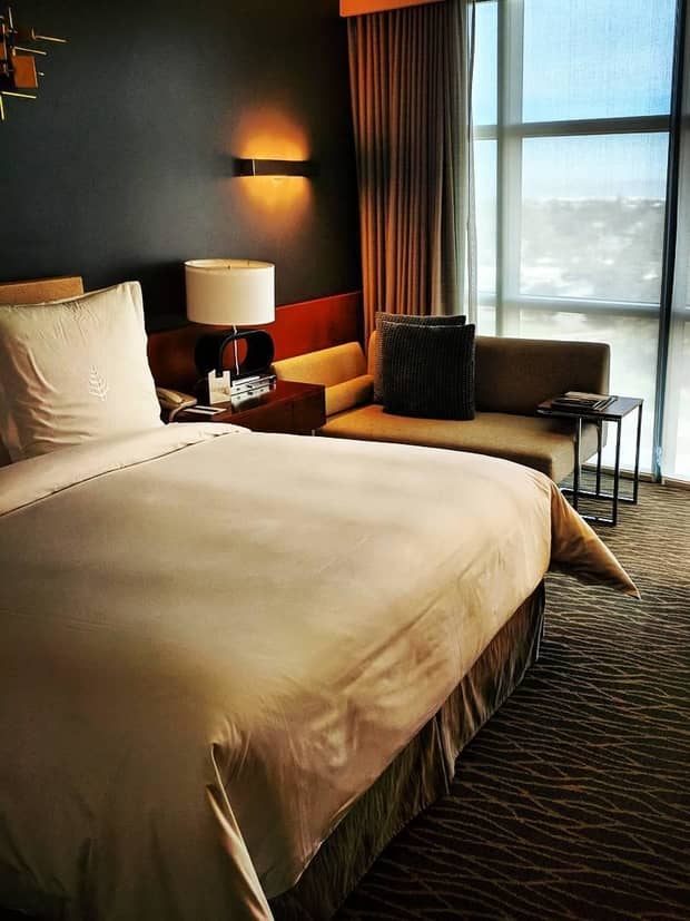 Corner of bed, lamp, gold chair under tall sunny window