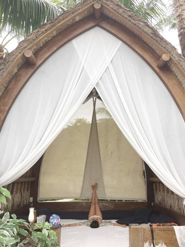 Woman does yoga stretch in outdoor pavilion with white curtains