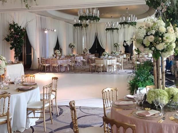 Elegant banquet tables with gold chairs and tall roses surrounding white dance floor