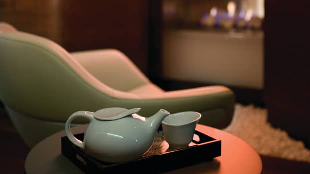 Modern white tea pot, cup on tray by leather chair, fireplace in background