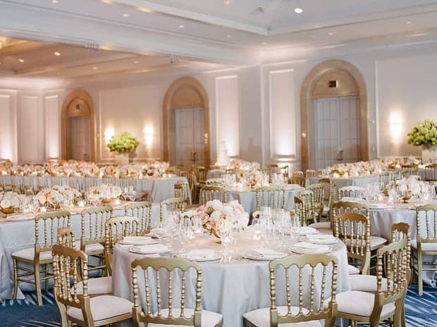 Ballroom wedding reception with gold chairs around round banquet tables 