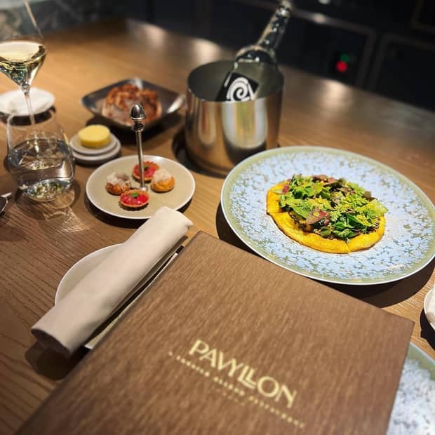 A Pavyllon menu on a wooden table surrounded by various culinary dishes