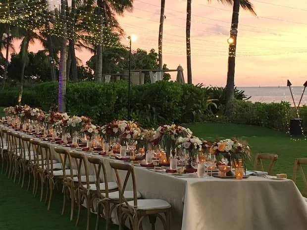 Long banquet wedding dining table with flowers, candles on lawn overlooking ocean